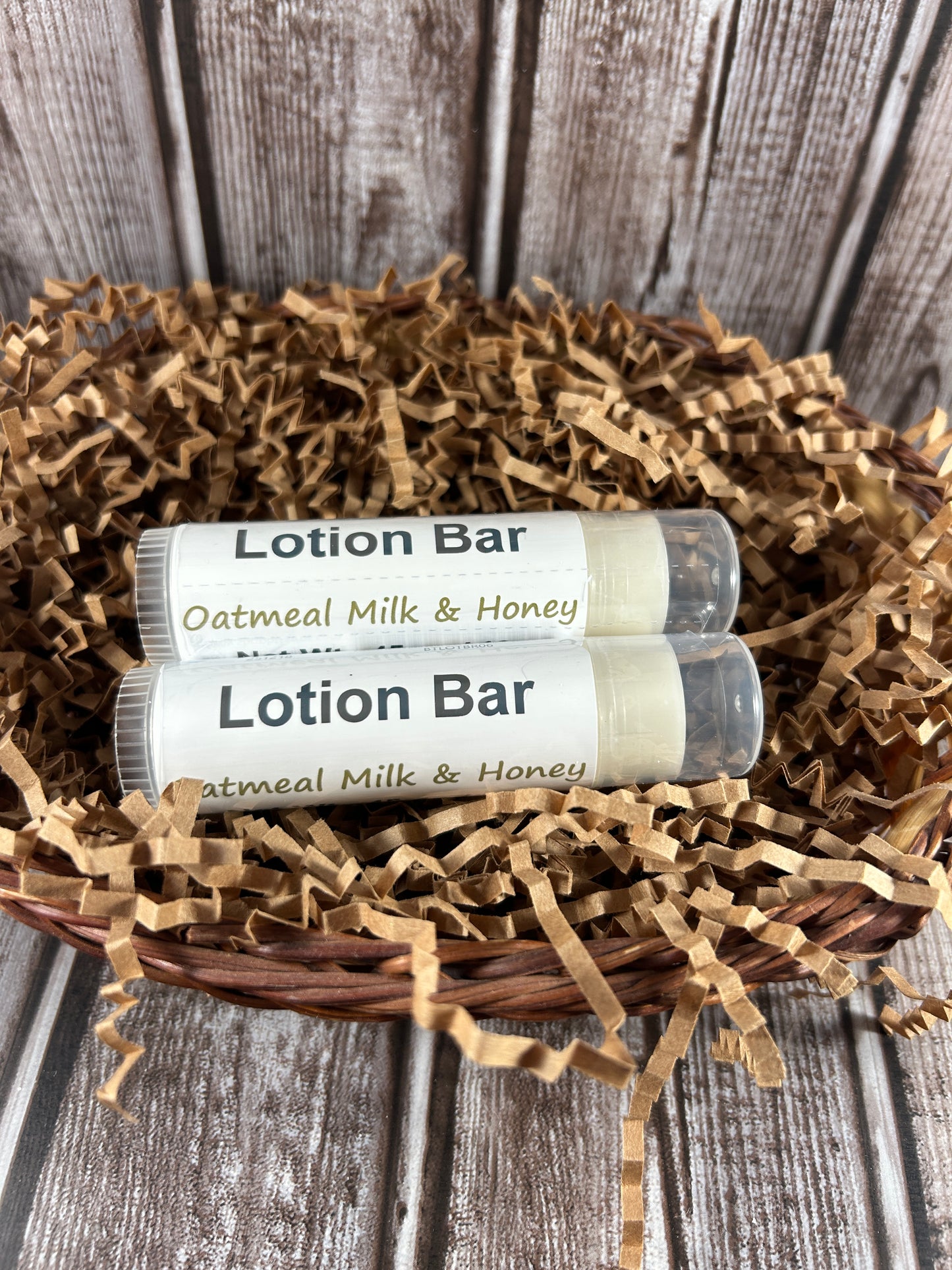 Two lotion bars labeled 'Oatmeal Milk & Honey' on a bed of straw against a wooden background.