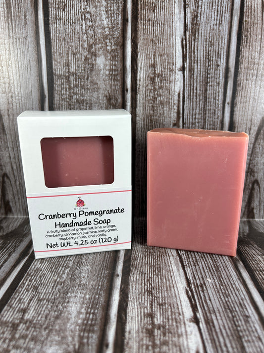 Bar of soap scented in cranbrry pomegranate, in a white box, against a wood grain background 