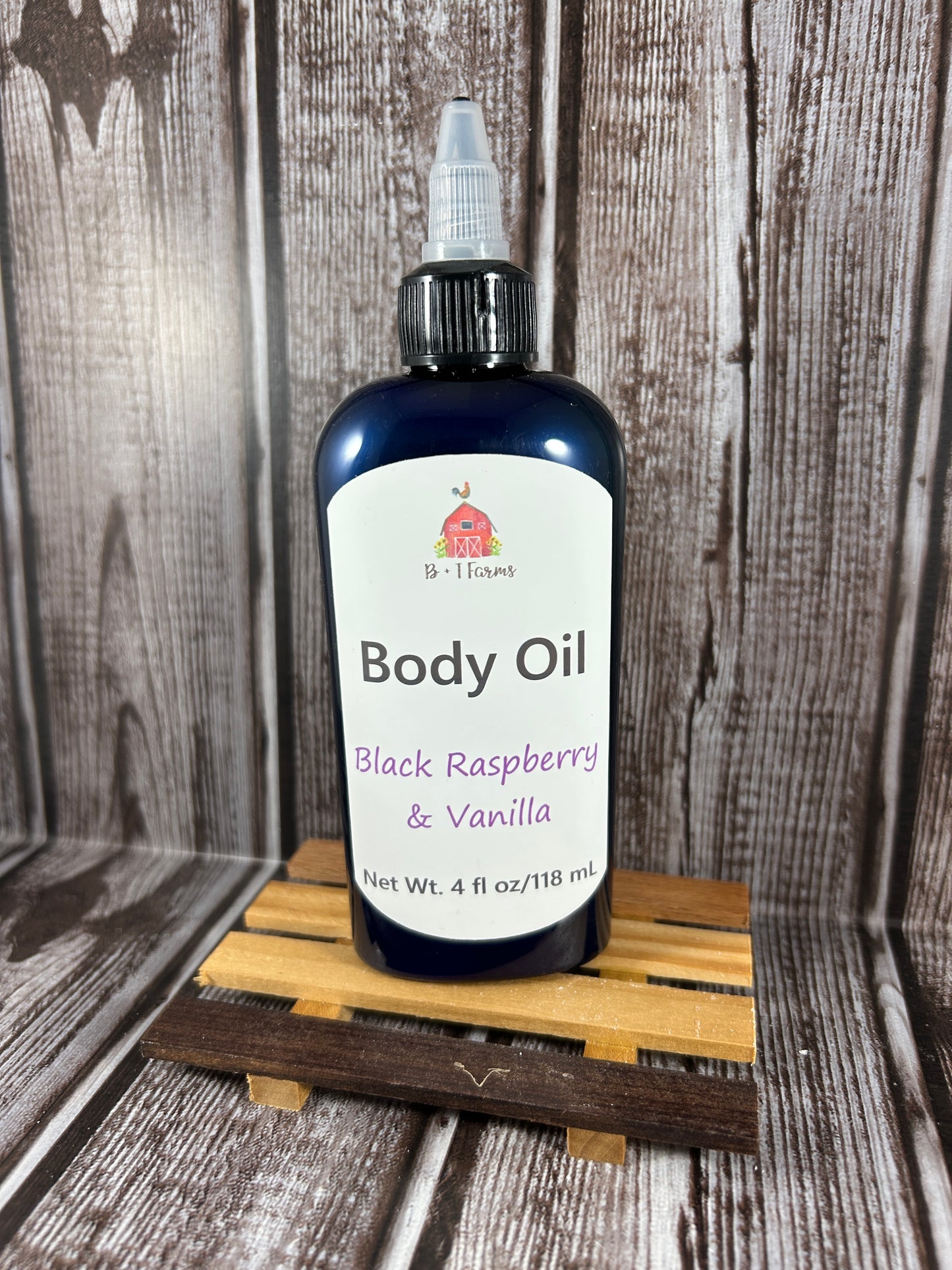 Body oil bottle labeled 'Black Raspberry & Vanilla' on a wooden surface