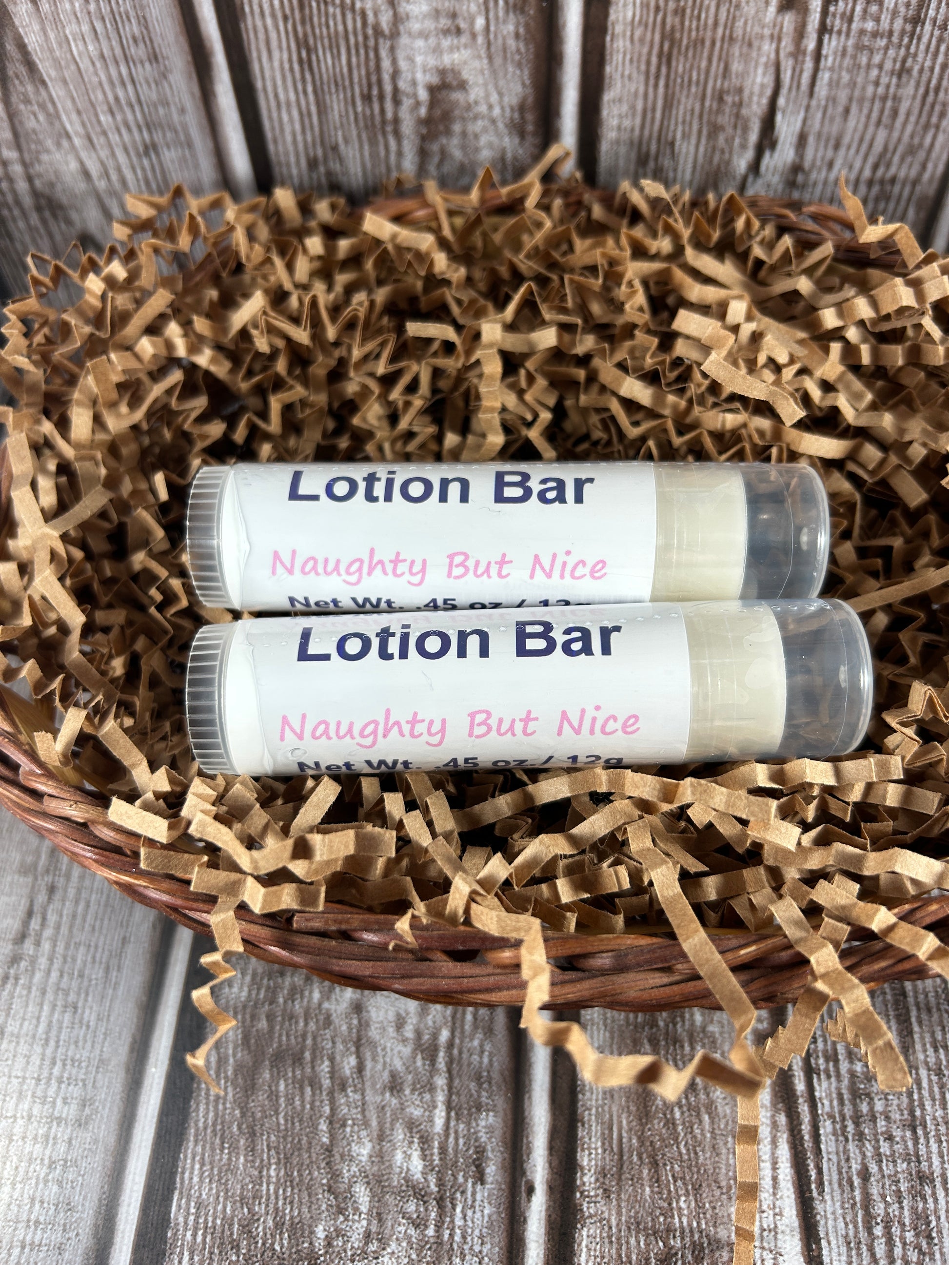 Two naughty but nice lotion bars in a basket with brown crinkle paper on a wooden surface