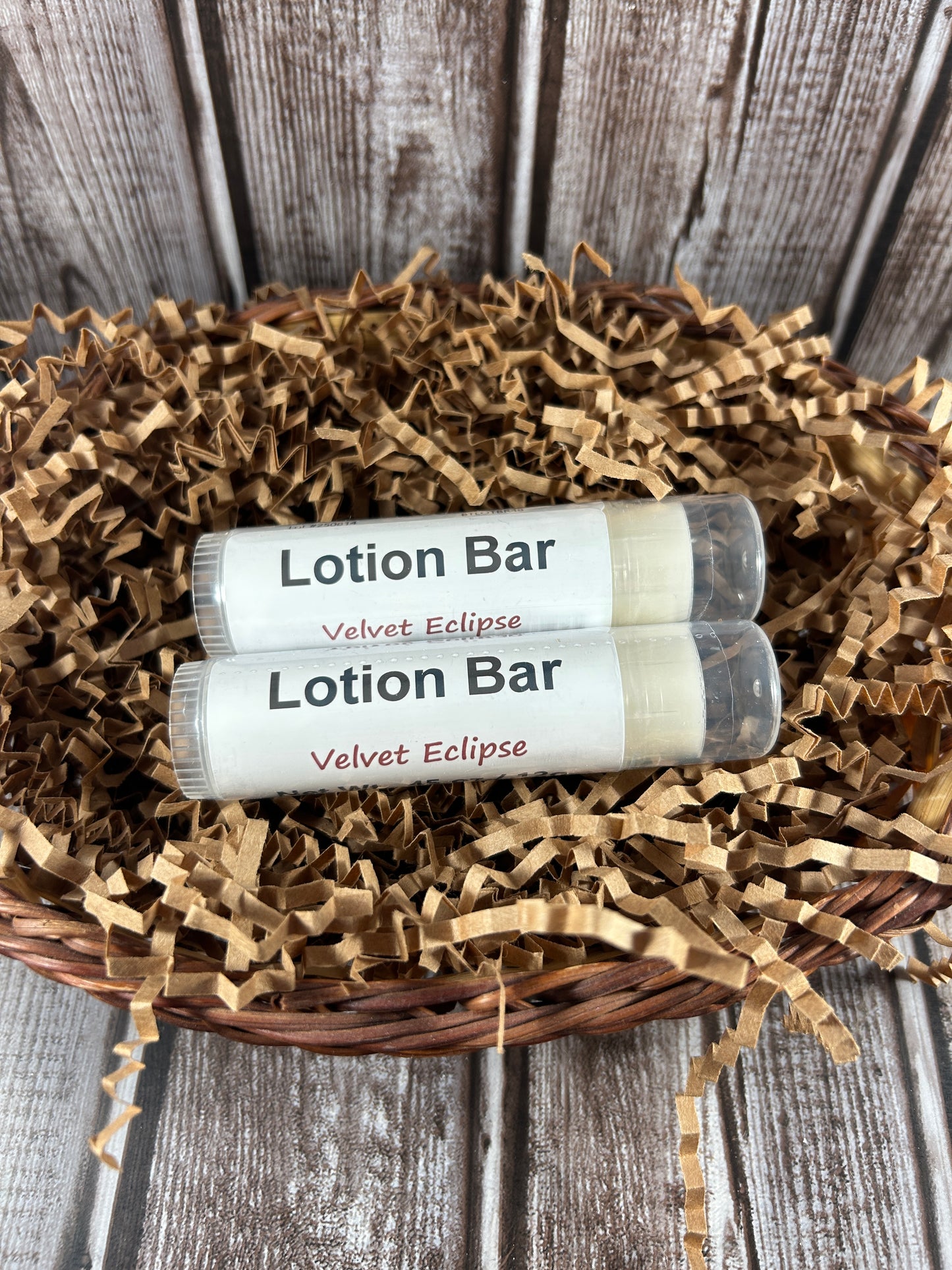 Two velvet eclipse lotion bars in a wicker basket with brown crinkle paper on a wooden surface.