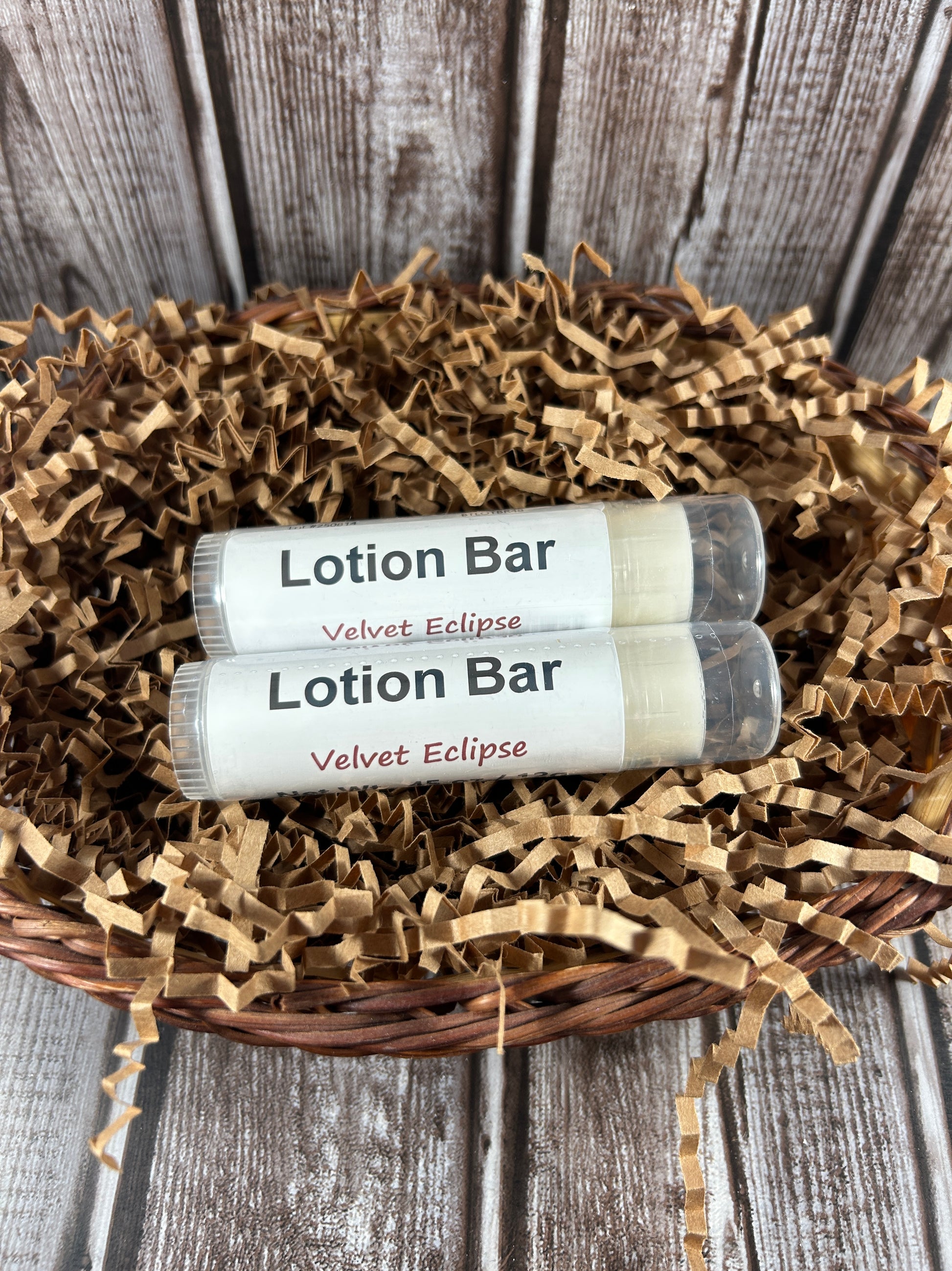 Two velvet eclipse lotion bars in a wicker basket with brown crinkle paper on a wooden surface.